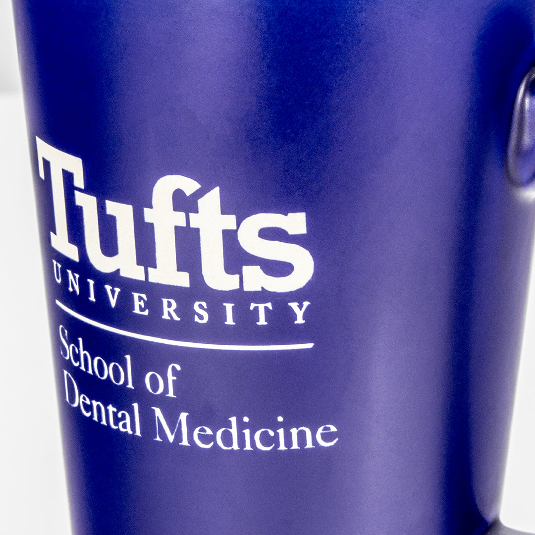 A close-up of a Blue with White Inside Ceramic Mug by Prize Possessions, featuring white text that reads Tufts University School of Dental Medicine.