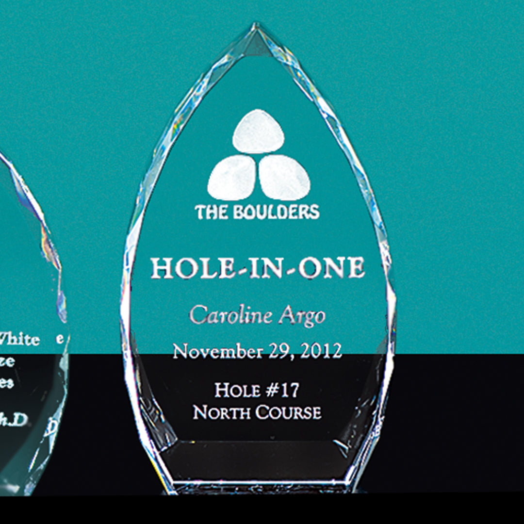 The Optic Crystal Award by Prize Possessions, engraved with The Boulders, HOLE-IN-ONE, Caroline Argo, November 29, 2012, Hole #17, North Course, gleams against teal—ideal for corporate awards or employee recognition.