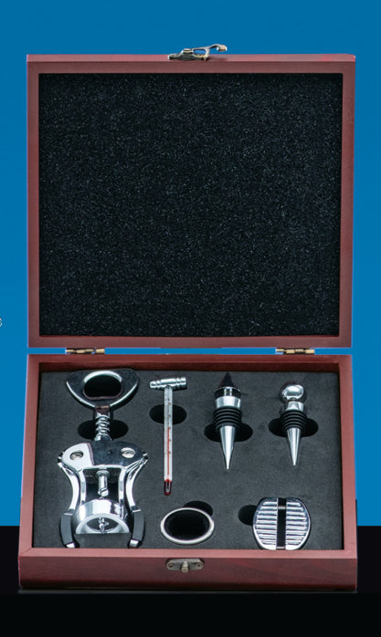 The Prize Possessions 6pc Wine Tool Set is displayed in a wooden box with a black interior, featuring a metal corkscrew, wine thermometer, pourer, foil cutter, and two bottle stoppers against a blue background.