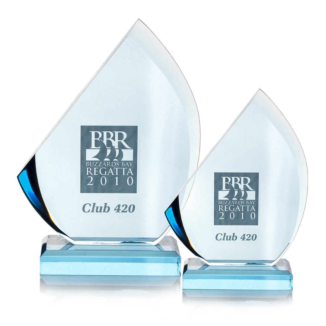 Two Prize Possessions Acrylic Blue Sail Awards feature sail-shaped acrylic designs with blue bases, engraved with "BBR Buzzards Bay Regatta 2010" and "Club 420." Displayed side by side, one award is larger than the other.