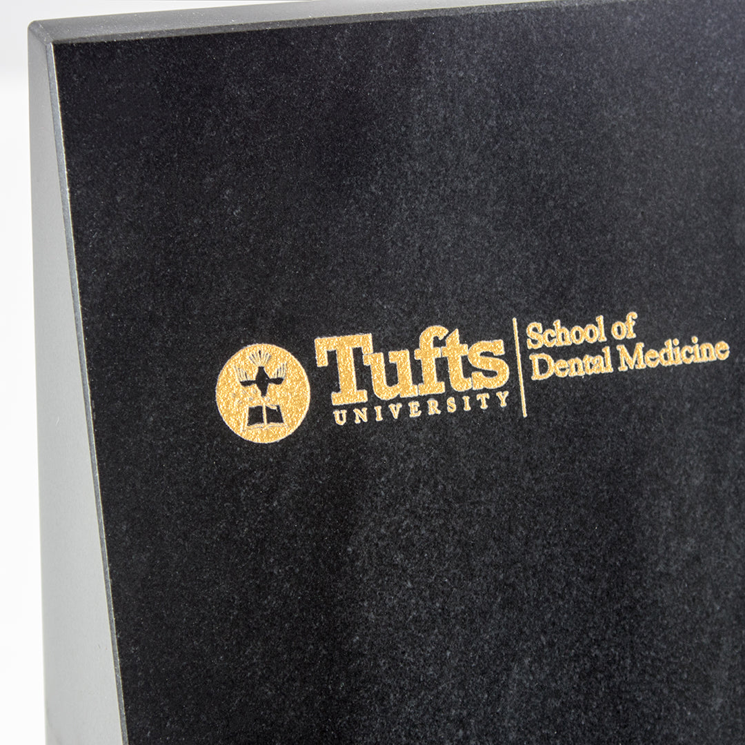 Close-up of a black plaque with the gold Tufts University School of Dental Medicine logo, styled beside Prize Possessions Black Marble Bookends for a modern home office decor touch.