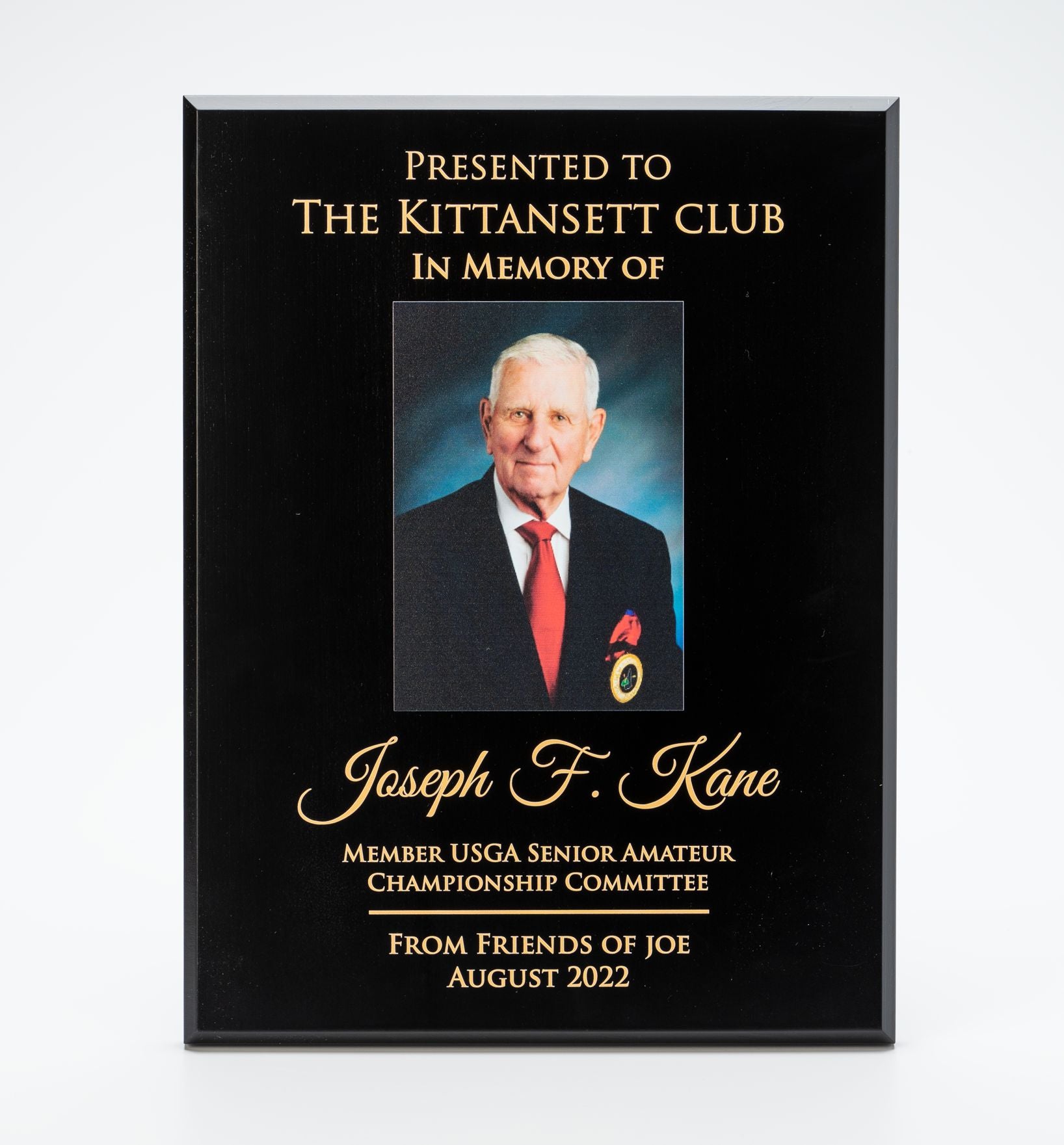 A Black Wood Plaque by Prize Possessions features a portrait of an older man in a suit and gold text: Presented to The Kittansett Club in memory of Joseph F. Kane, USGA Senior Amateur Championship Committee, From Friends of Joe, August 2022.