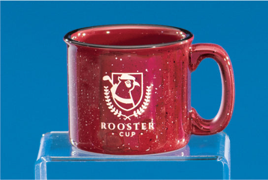 A Burgundy Campfire Mug by Prize Possessions with black speckles and a white Rooster Cup logo sits on a clear stand against a blue background.
