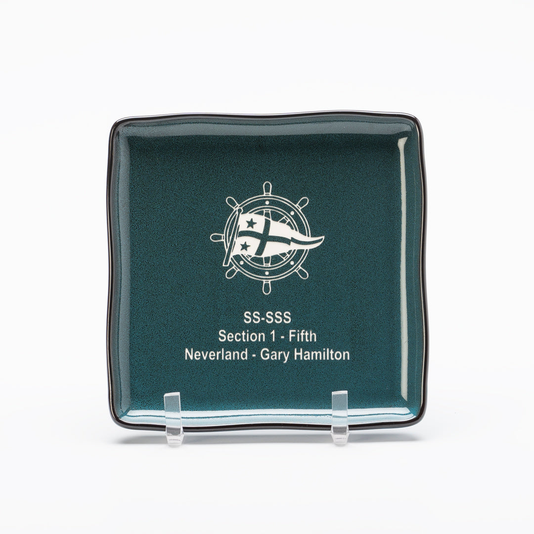 A modern dinnerware piece, the Ceramic Midnight Blue Square Plate by Prize Possessions features a nautical emblem and stars and is inscribed with “SS-SSS Section 1 - Fifth Neverland · Gary Hamilton.” Display it on a stand for added elegance.
