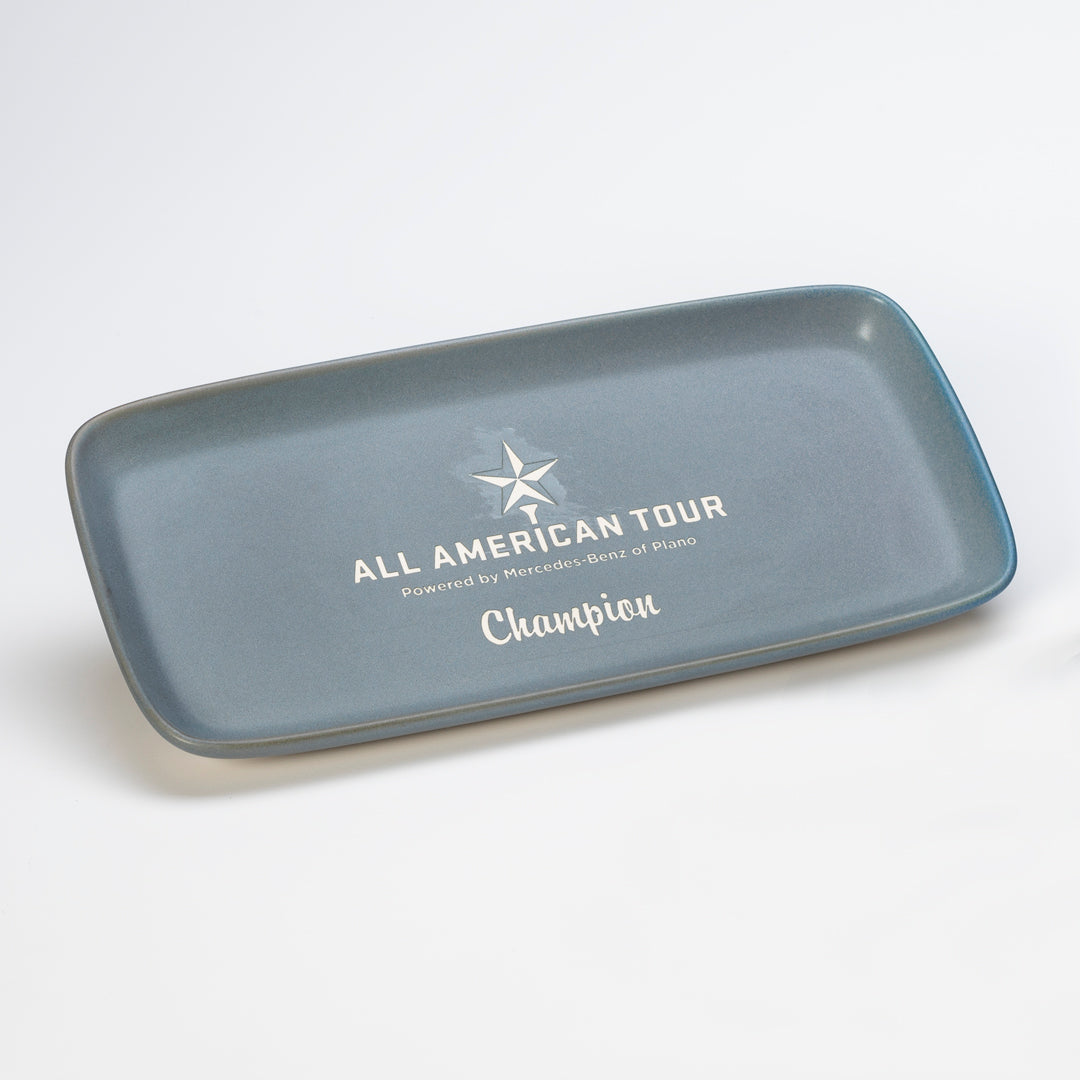 The Prize Possessions Ceramic Nevada Gray/Sand Strata Platter features “ALL AMERICAN TOUR Powered by Mercedes-Benz of Plano,” “Champion,” and a star logo—an elegant choice for any modern table setting.