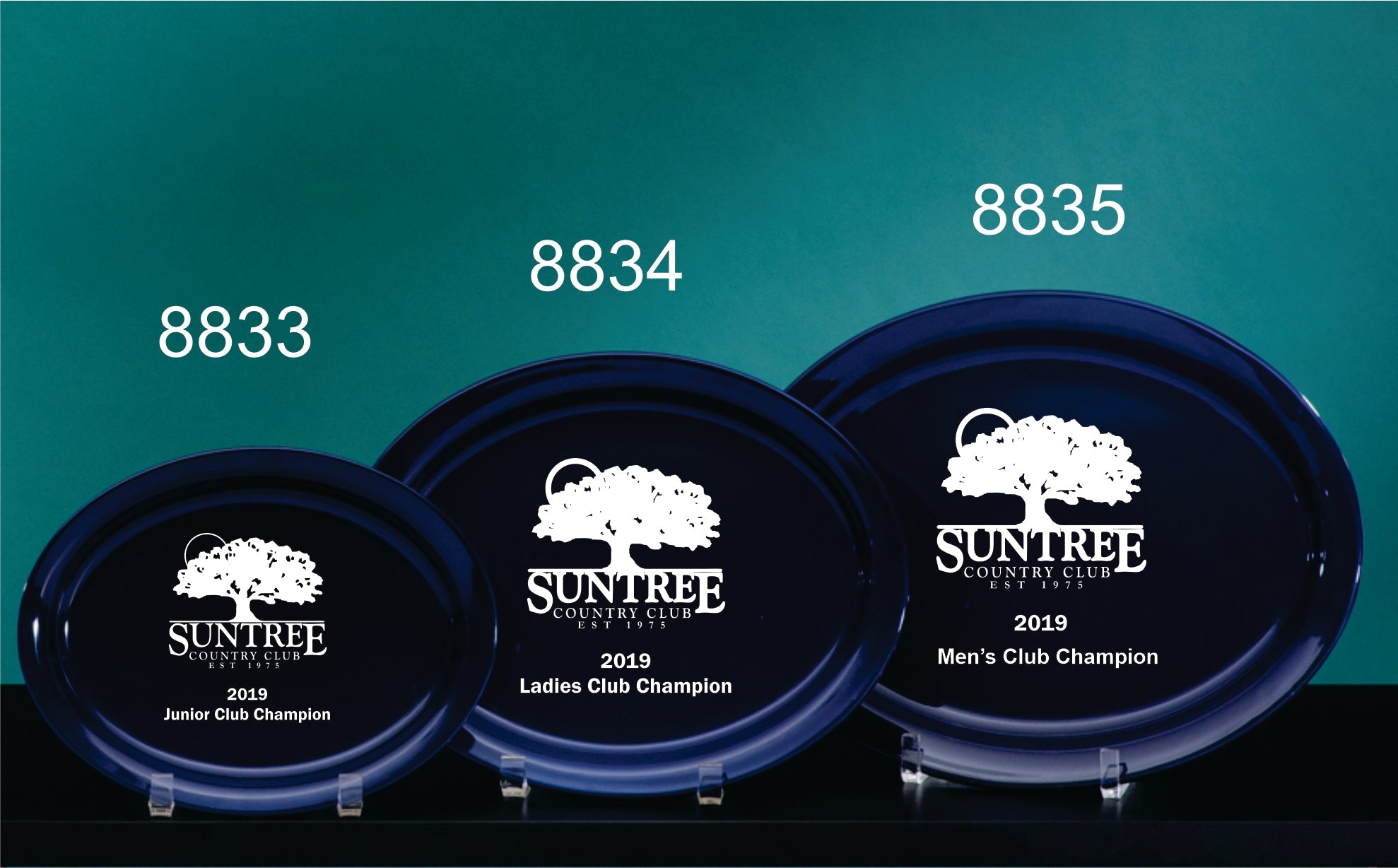 Three Prize Possessions Cobalt Ceramic Narrow Rim Platters, blue and glass-like, each engraved with Suntree Country Club for 2019 Junior, Ladies, and Mens Club Champion awards, displayed on stands against a teal background.
