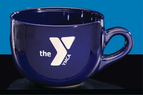 The Cobalt Latte Mug by Prize Possessions is a dark blue ceramic mug with a handle, featuring the white YMCA logo and "the" on the front—a stylish choice for coffee lovers.