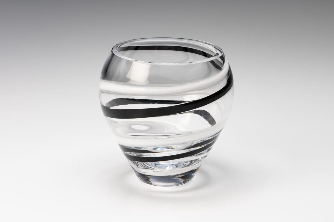 The Prize Possessions Crystal Bowl with a striking spiral design of bold black and white stripes stands out as a unique decorative piece against a plain, light gray background.