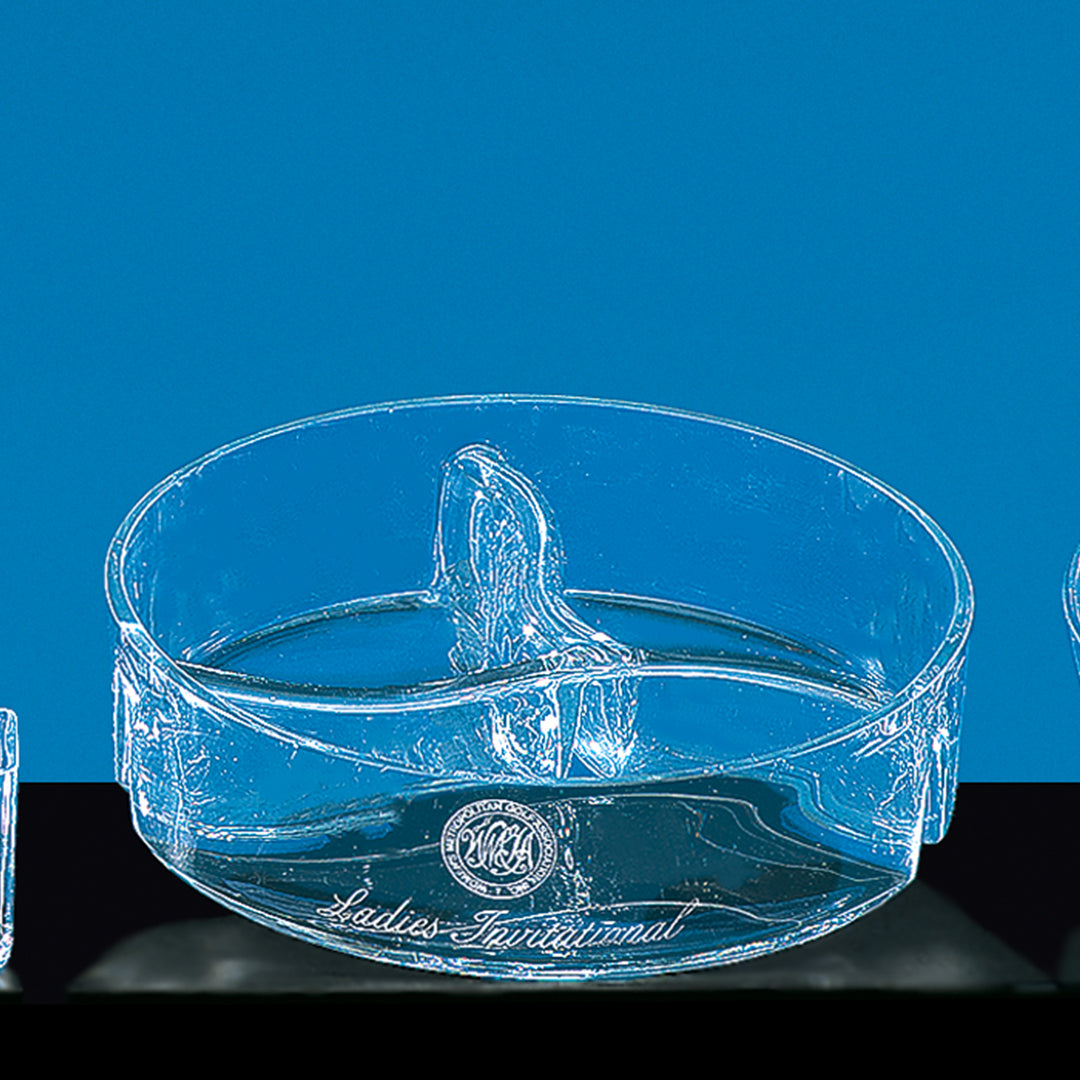 A clear Crystal Chip/Dip Tray by Prize Possessions, featuring a raised center divider, is shown against a blue background. The tray is engraved with "Ladies Invitational" and has an emblem on the side.