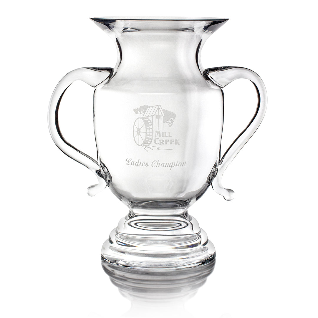 The Prize Possessions Crystal Darlington Vase is a clear glass trophy cup with two handles, engraved with a mill logo and “Mill Creek Ladies Champion,” featuring a wide mouth, rounded base, and elegant pedestal design.