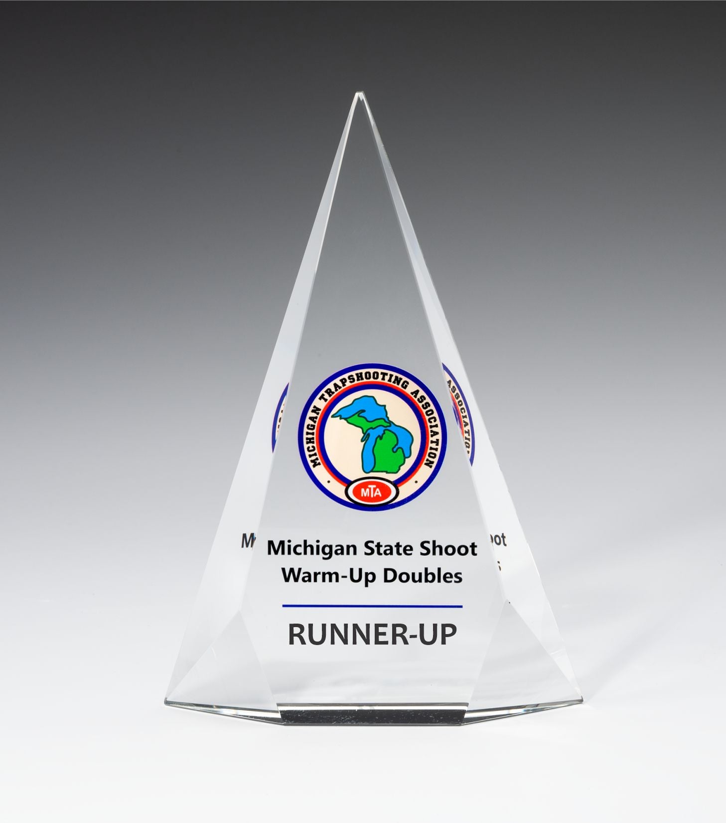 The Crystal Facet Triangle by Prize Possessions is a clear, pyramid-shaped crystal award with the Michigan Trapshooting Association logo and "Michigan State Shoot Warm-Up Doubles RUNNER-UP"—an impressive employee recognition or corporate gift.