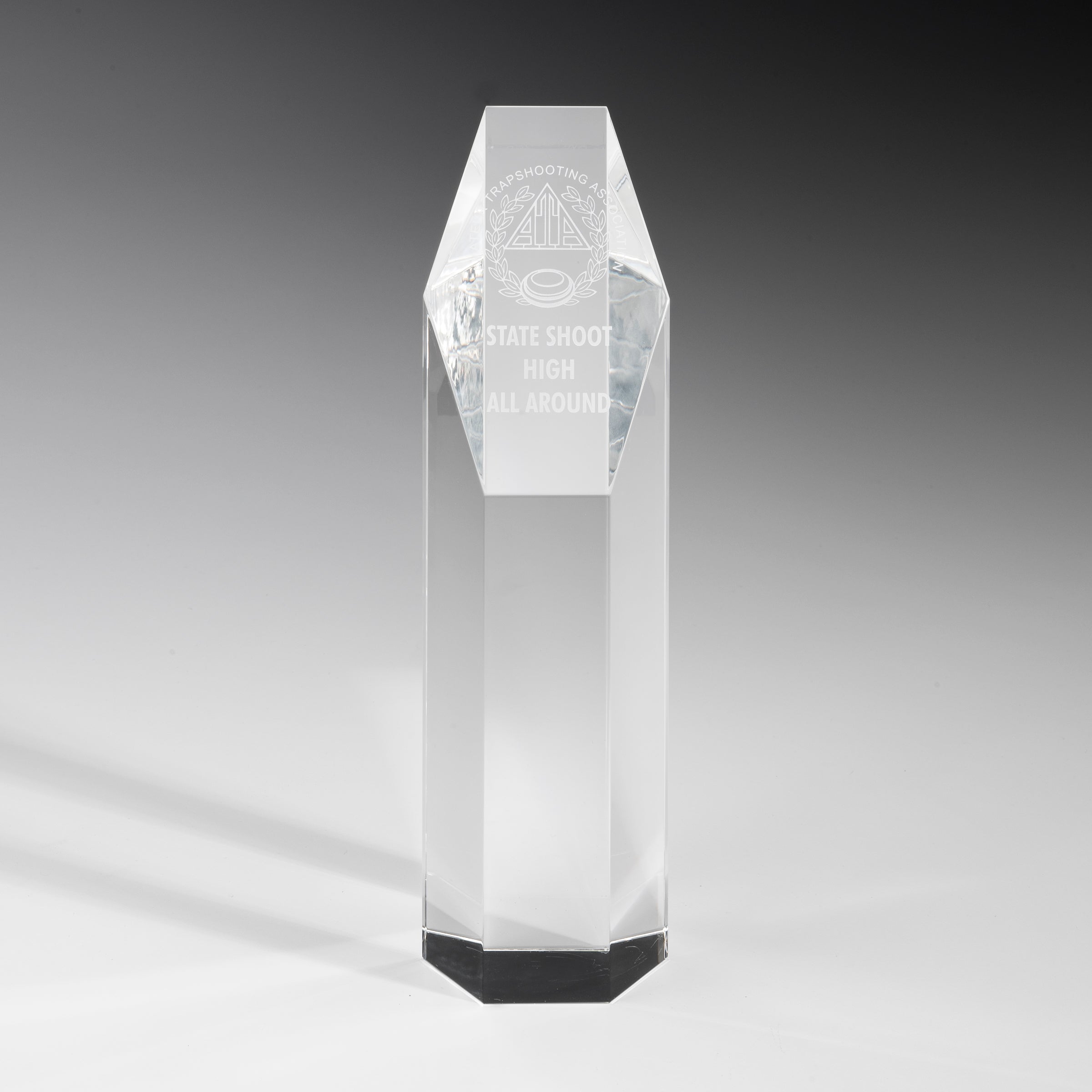 The Crystal Hexagon Award by Prize Possessions is a tall, clear engraved crystal trophy with an octagonal base and pointed top, ideal for corporate recognition. It stands on a white surface with a gray gradient background.