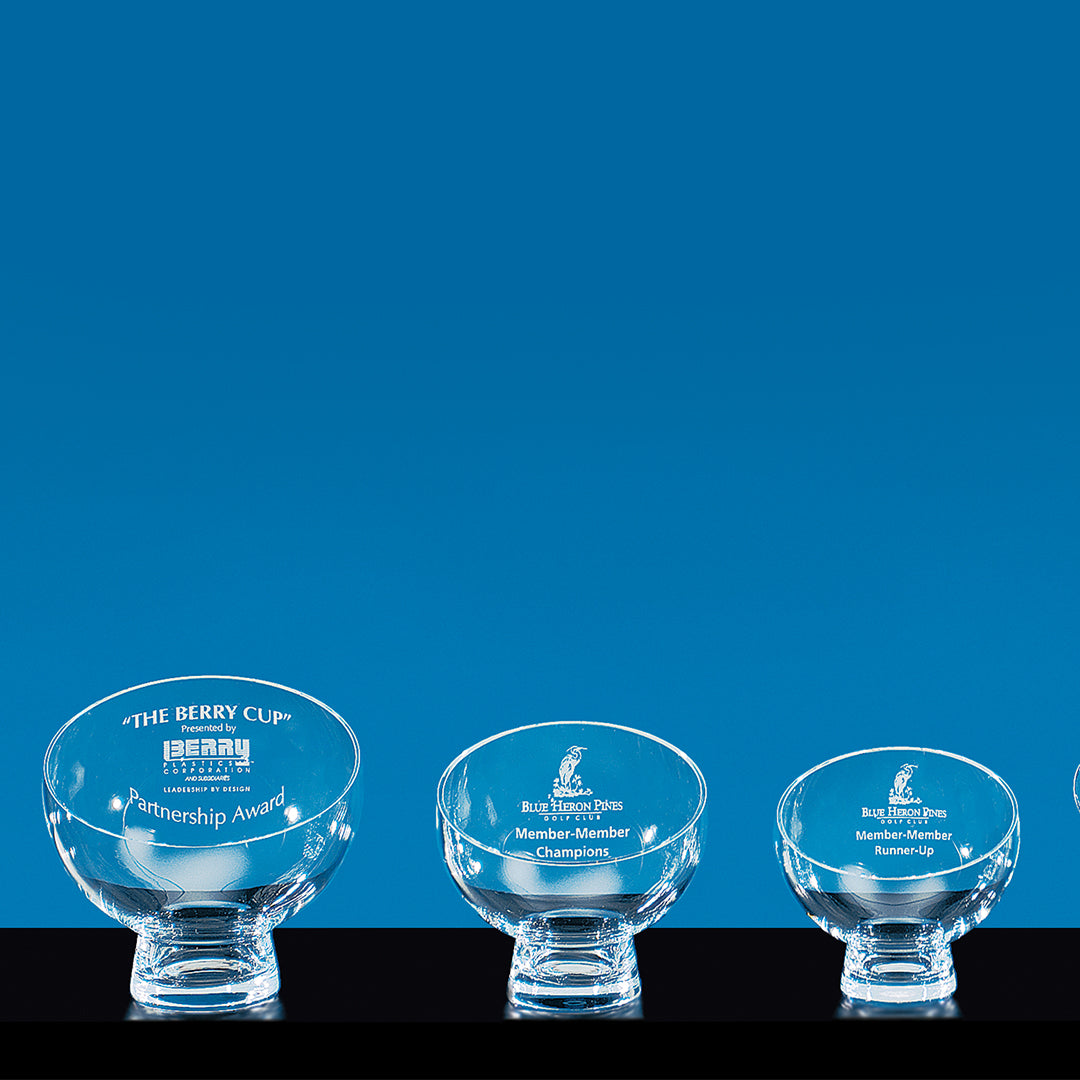 Four Prize Possessions Crystal Luna Bowls of different sizes are arranged in a row on a blue background, each engraved with unique golf tournament titles—an impressive choice for a trophy or elegant centerpiece.