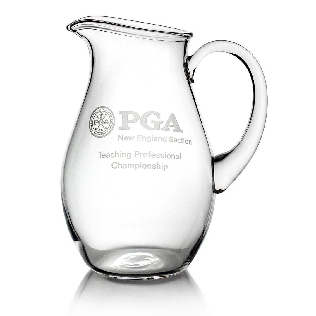 The Crystal Pitcher by Prize Possessions is an elegant, empty crystal glassware piece with a handle and spout, engraved with the PGA New England Section Teaching Professional Championship logo and text. Perfect for serving beverages.