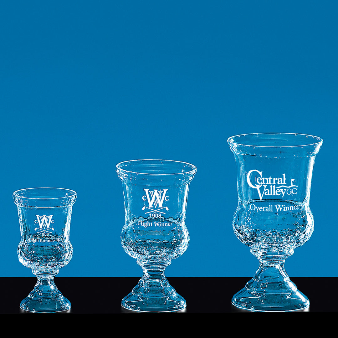 The Crystal Warrington Trophy by Prize Possessions is shown in three sizes against a blue background. Each clear crystal cup features engraved text, ideal for corporate awards or recognition ceremonies.