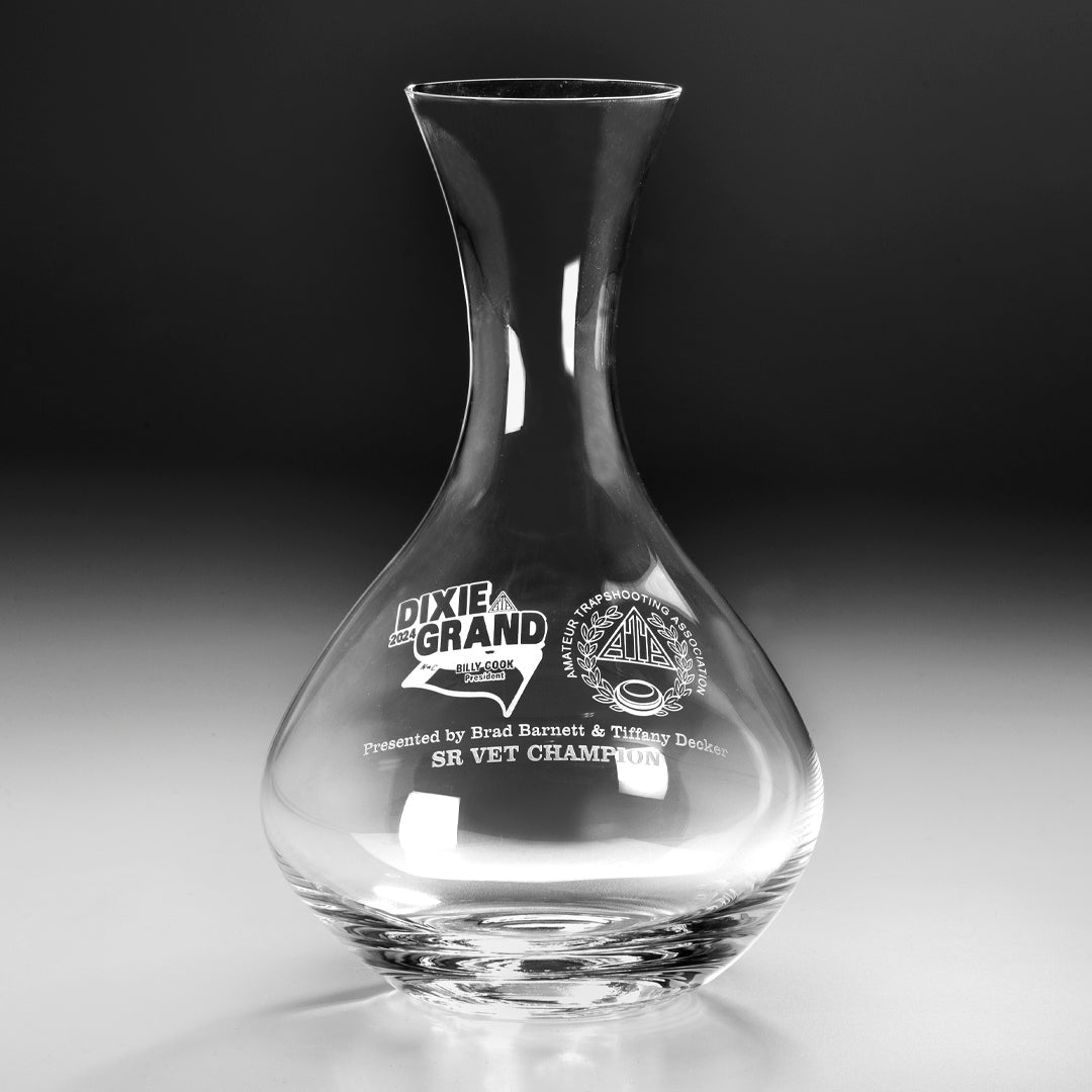 The Prize Possessions Crystal Wine Decanter, etched with text and logos like Dixie Grand, NSGA, and SR Vet Champion, is showcased on a smooth grey background—an elegant gift for wine collectors.