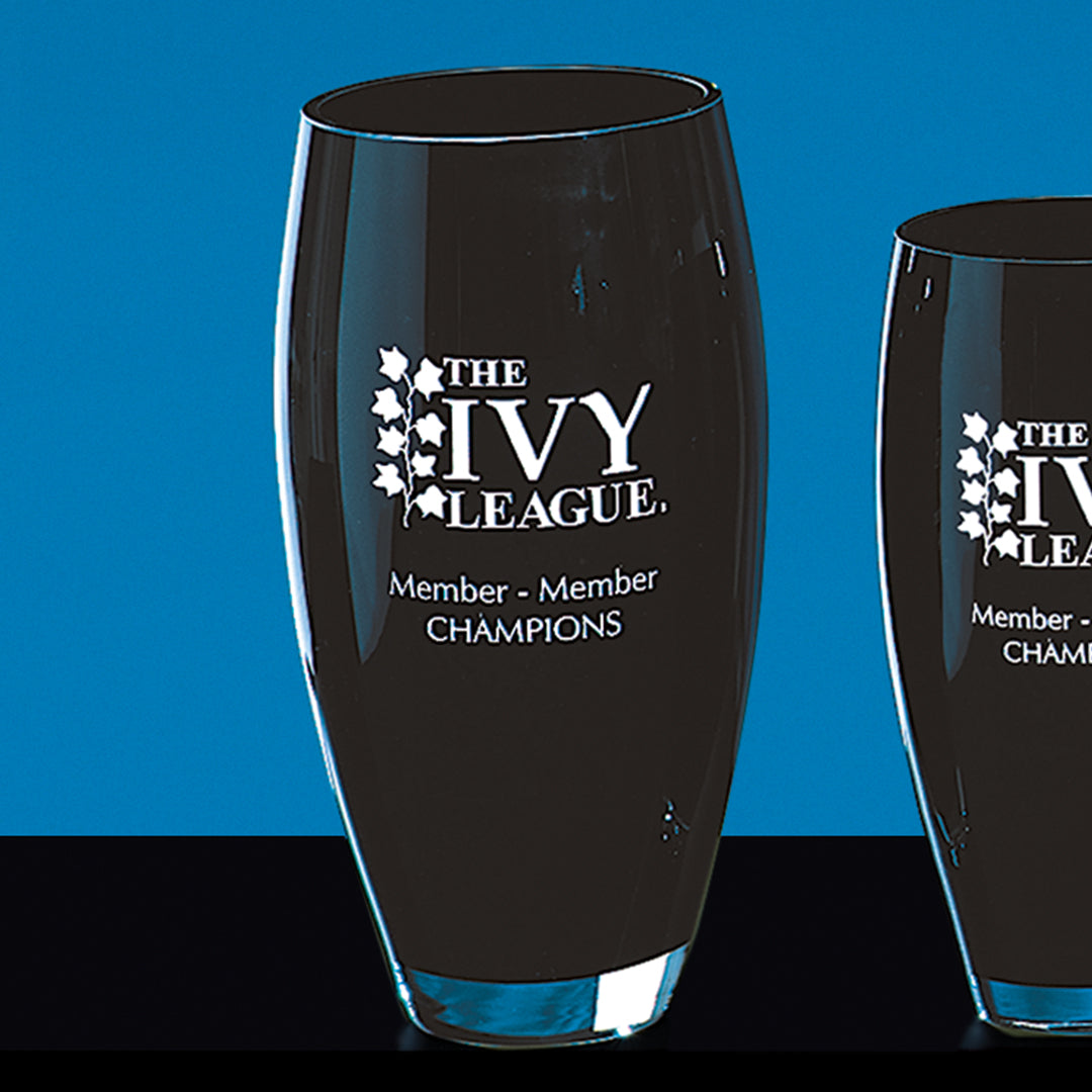 Two Ebony Crystal Vases by Prize Possessions, with "The Ivy League Member Member Champions" engraved on the front, are displayed on a black surface against a blue background.