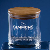 The Prize Possessions Glass Jar with Wood Cover, engraved "Simmons Field Hockey 2019 Most Valuable Player Lucy McNamara," is displayed against a blue background.