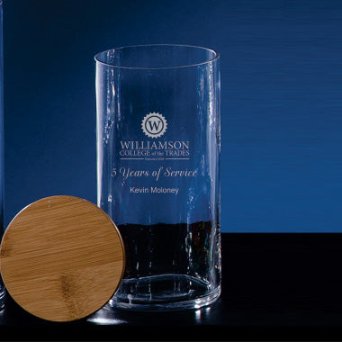 A Prize Possessions Glass Jar with Wood Cover sits on a dark surface, engraved in white with "Williamson College of the Trades, 5 Years of Service, Kevin Moloney" against a blue background.