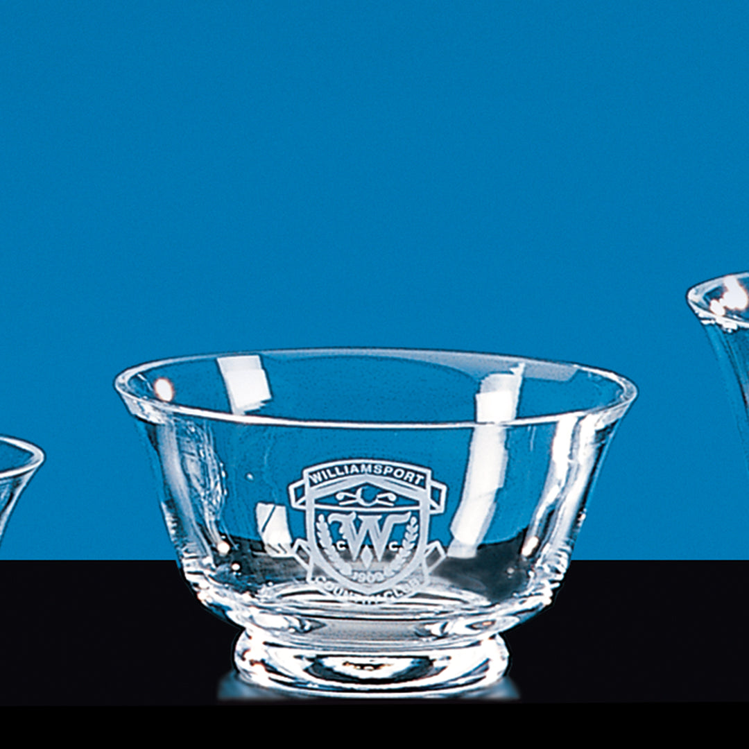 The Glass Revere Bowl by Prize Possessions features a wide rim, pedestal base, and engraved Williamsport crest, making it a stunning decorative accent against a blue background.