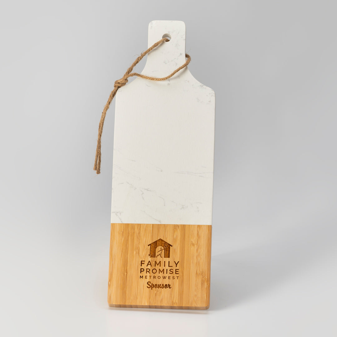 The Prize Possessions Marble/Wood Serving Board has a white top, natural wood bottom, rope loop, and an engraved “Family Promise MetroWest Sponsor” logo on the lower section.