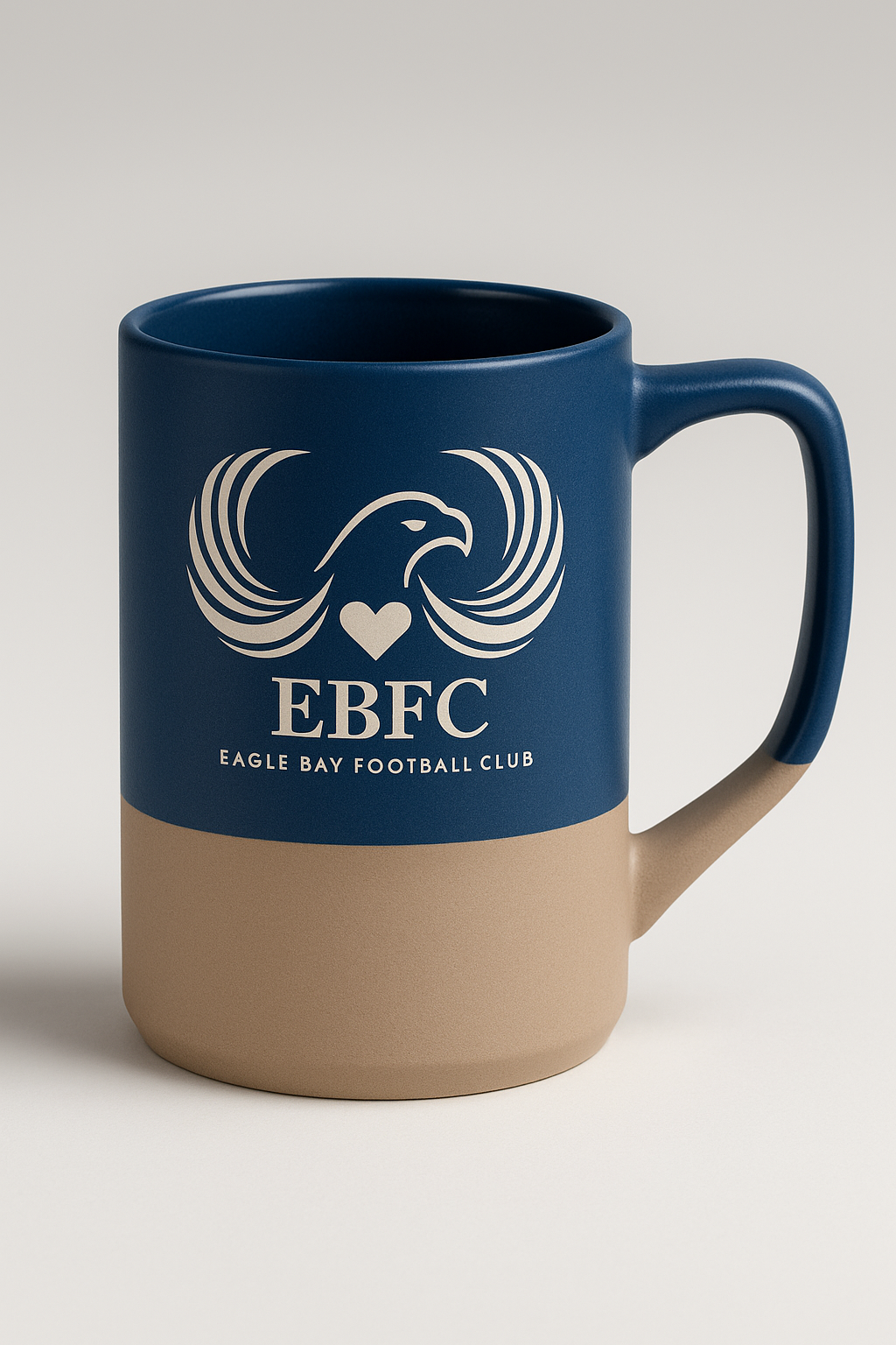 The Prize Possessions Midnight Blue Ceramic Mug with Gray Base is a stylish everyday mug featuring an eagle logo, heart, EBFC letters, and Eagle Bay Football Club printed underneath.