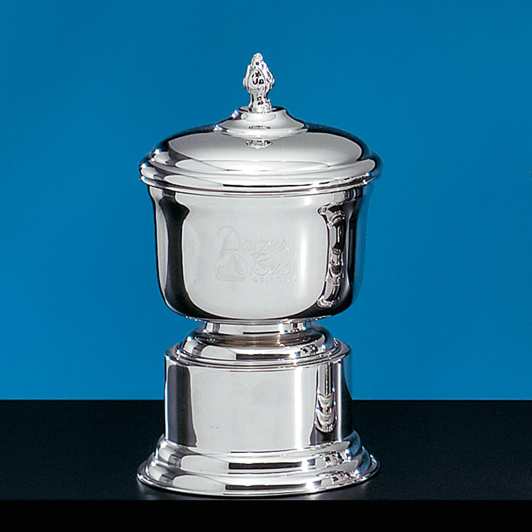 The Nickle Plate Beaumont Award by Prize Possessions is a shiny silver trophy with a lid and ornate finial, shown on a black surface against a blue background. Perfect for corporate or academic ceremonies, it features engraved front text.