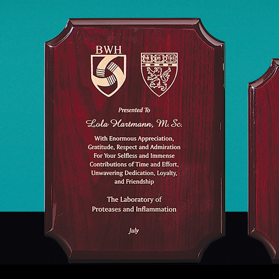 The Prize Possessions Notched Rosewood Plaque, featuring two crests and an inscription, honors Lola Hartmann, M.Sc., for her outstanding dedication, loyalty, and leadership in Proteases and Inflammation—presented in July.