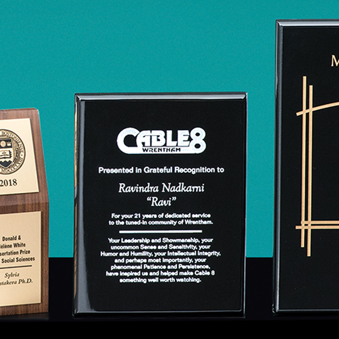 Three corporate awards sit on a teal background. The center Piano Finish Black Plaque by Prize Possessions honors Ravindra Nadkami for 21 years with Cable 8 Wrentham, commending his leadership and integrity.