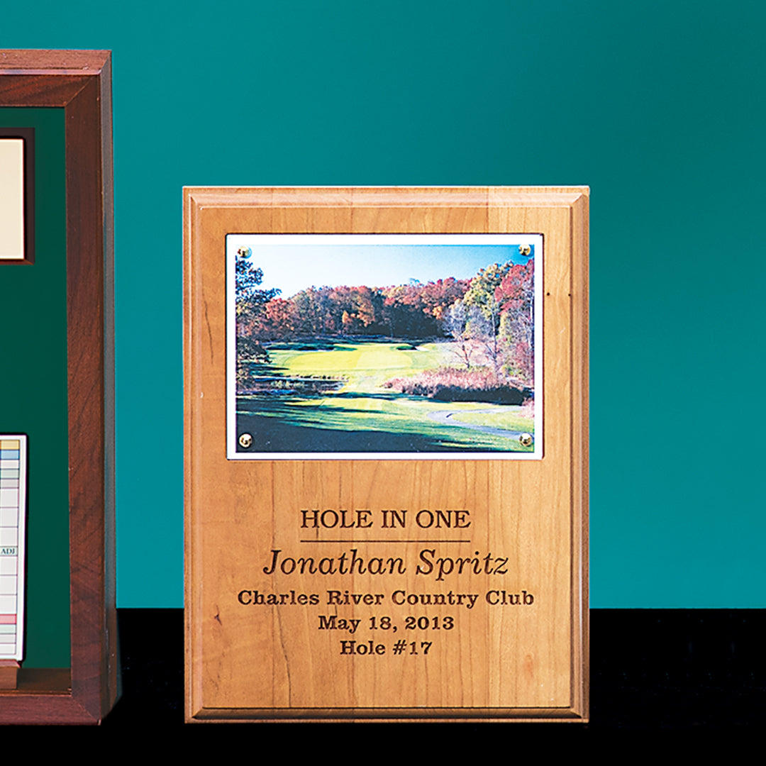 The Prize Possessions Plaque with Photo Insert displays a golf course photo and engraved text: “HOLE IN ONE Jonathan Spritz Charles River Country Club May 18, 2013 Hole #17,” shown upright against a teal backdrop.