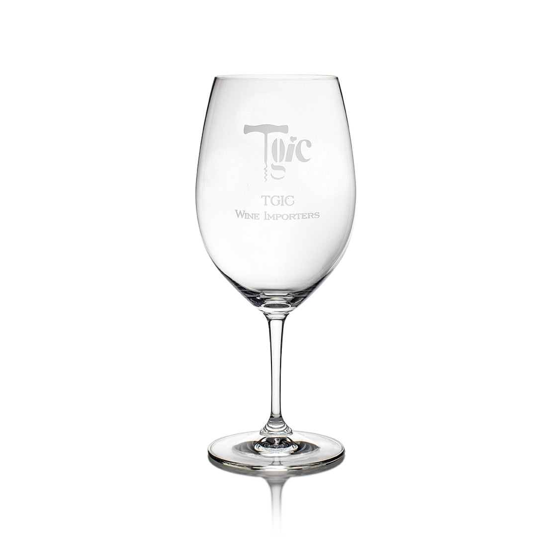 A clear, empty Riedel Restaurant Wine Glass by Prize Possessions stands on a white background, highlighting premium crystal glassware with the TGIC Wine Importers logo etched on the bowl.