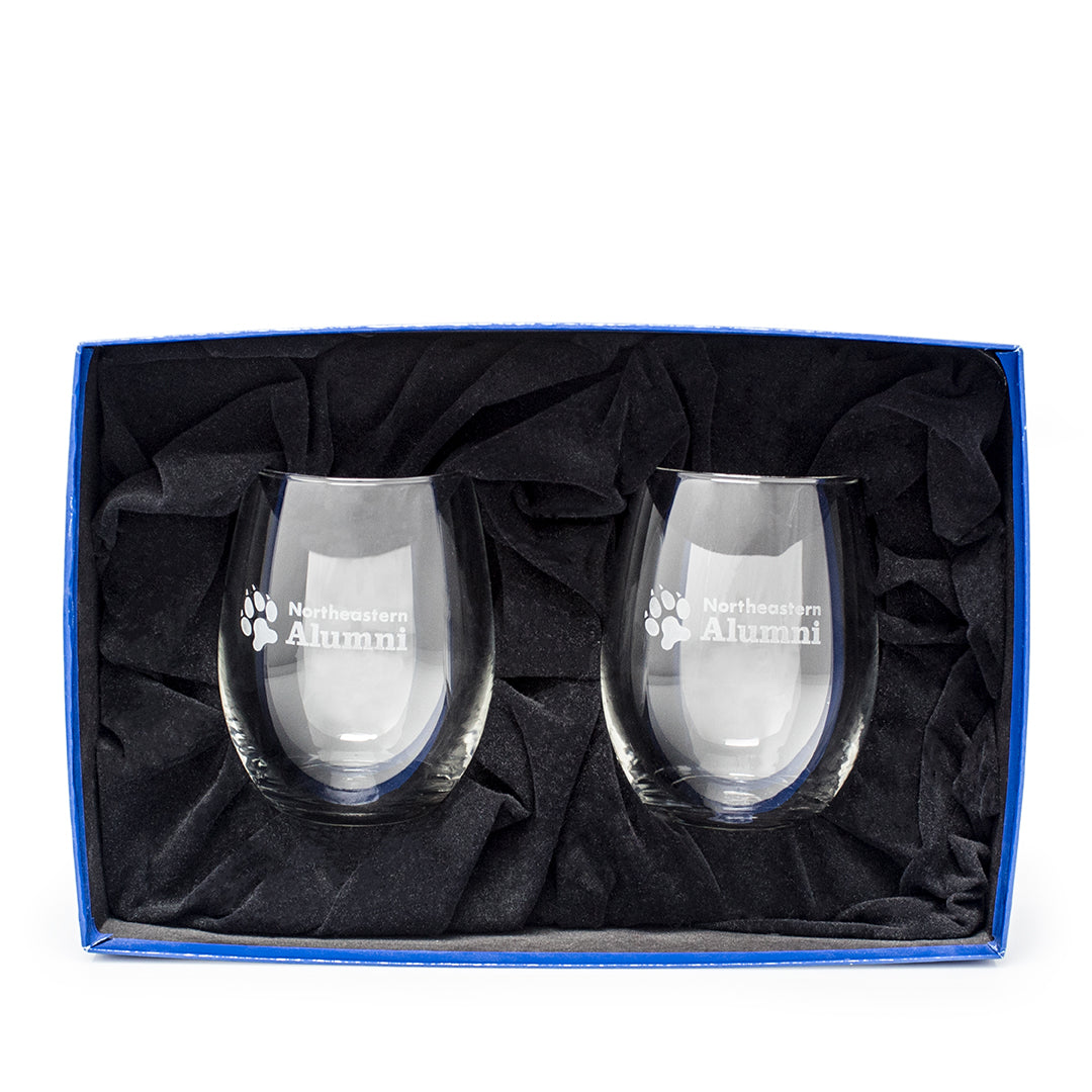 A blue box contains two Prize Possessions Riedel Stemless Gift Set glasses, each etched with a paw print and "Northeastern Alumni," resting on black fabric.