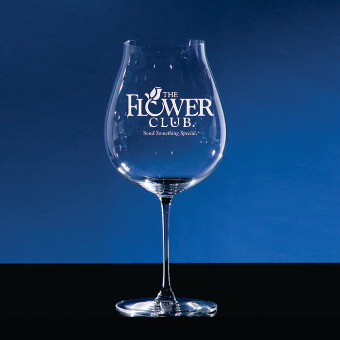 A Riedel Veritas Pinot Noir Glass by Prize Possessions sits on a dark surface, with THE FLOWER CLUB and Send Something Special. printed in white on the bowl, set against a blue backdrop.