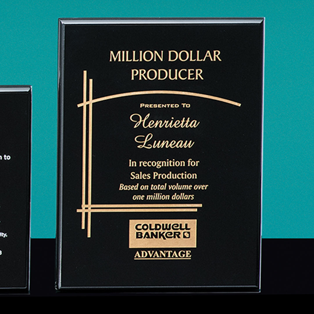 The Prize Possessions Rosewood Plaque in black and gold reads "Million Dollar Producer" and "Presented to Henrietta Luneau for Sales Production," featuring the Coldwell Banker Advantage logo at the bottom.