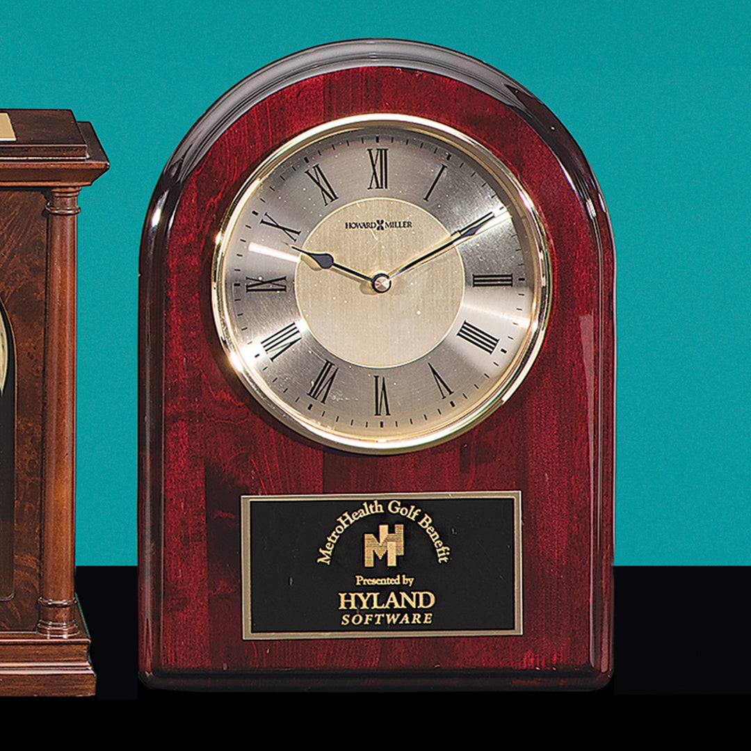 The Rosewood Wall Clock by Prize Possessions features a silver face with Roman numerals and a black and gold plaque reading, Mashfields Golf Classic Presented by Hyland Software—an elegant choice for reliable timekeeping.
