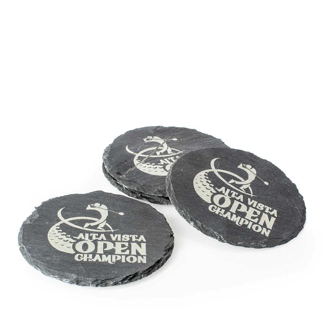 The Prize Possessions Round Slate Coaster Set of 4, featuring “ALTA VISTA OPEN CHAMPION” golf engraving, includes three stacked and one separate coaster, ideal as a stylish table accessory for protecting surfaces.