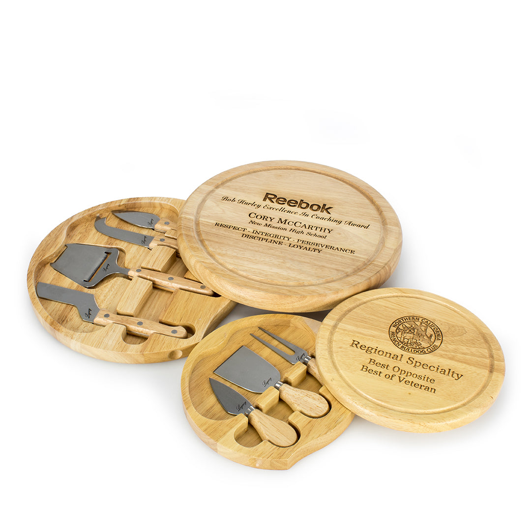 Three Prize Possessions Round Wood Cheese Boards with Tools are displayed. Two feature engraved awards, while one is open to show four stainless steel cheese knives and serving tools neatly arranged inside.
