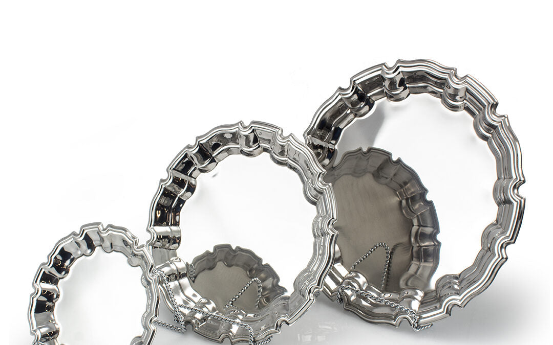 The Silverplate Scalloped Tray by Prize Possessions features four nested, scalloped-edge trays in varying sizes with a reflective finish, displayed on a white background and accented with a draped chain—ideal for serving or as a decorative centerpiece.