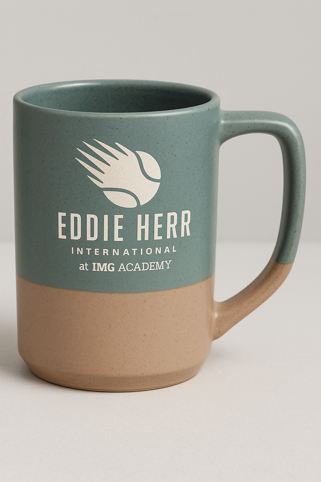 The Prize Possessions Slate Ceramic Mug with a gray base features the Eddie Herr International at IMG Academy logo with a stylized tennis ball, making it perfect for everyday use.