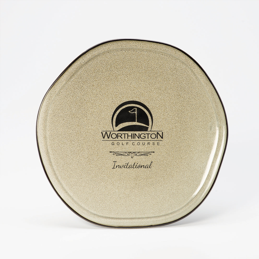 The Stoneware Ash Plate by Prize Possessions is a round, beige plate with a speckled finish and black trim, featuring the Worthington Golf Course logo and "Invitational" printed in black—a stylish, compact accessory.