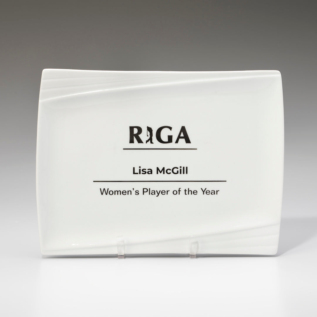 A White Ceramic Pacific Platter by Prize Possessions, displayed on a stand, features the RIGA logo and the inscription: Lisa McGill, Women's Player of the Year.
