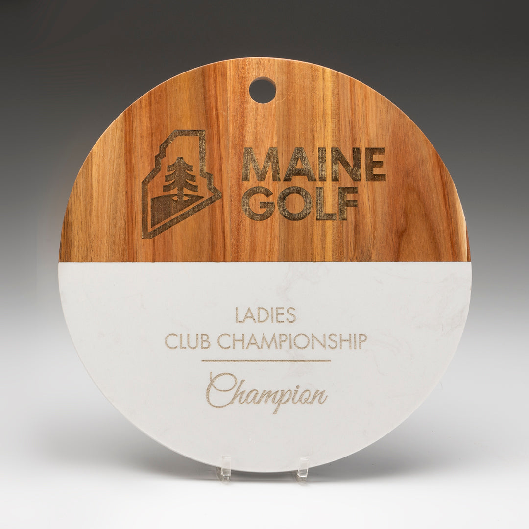 The Prize Possessions White Marble/Acacia Round Wood Board features MAINE GOLF and a tree logo engraved at the top, with "Ladies Club Championship Champion" below—ideal as a distinctive cheese or charcuterie board.