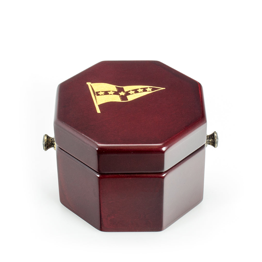 The Prize Possessions Wood Case Clock comes in a small, octagonal, dark red wood box with brass hinges and a gold flag emblem with three stars and a chevron on the lid, shown on a plain white background.