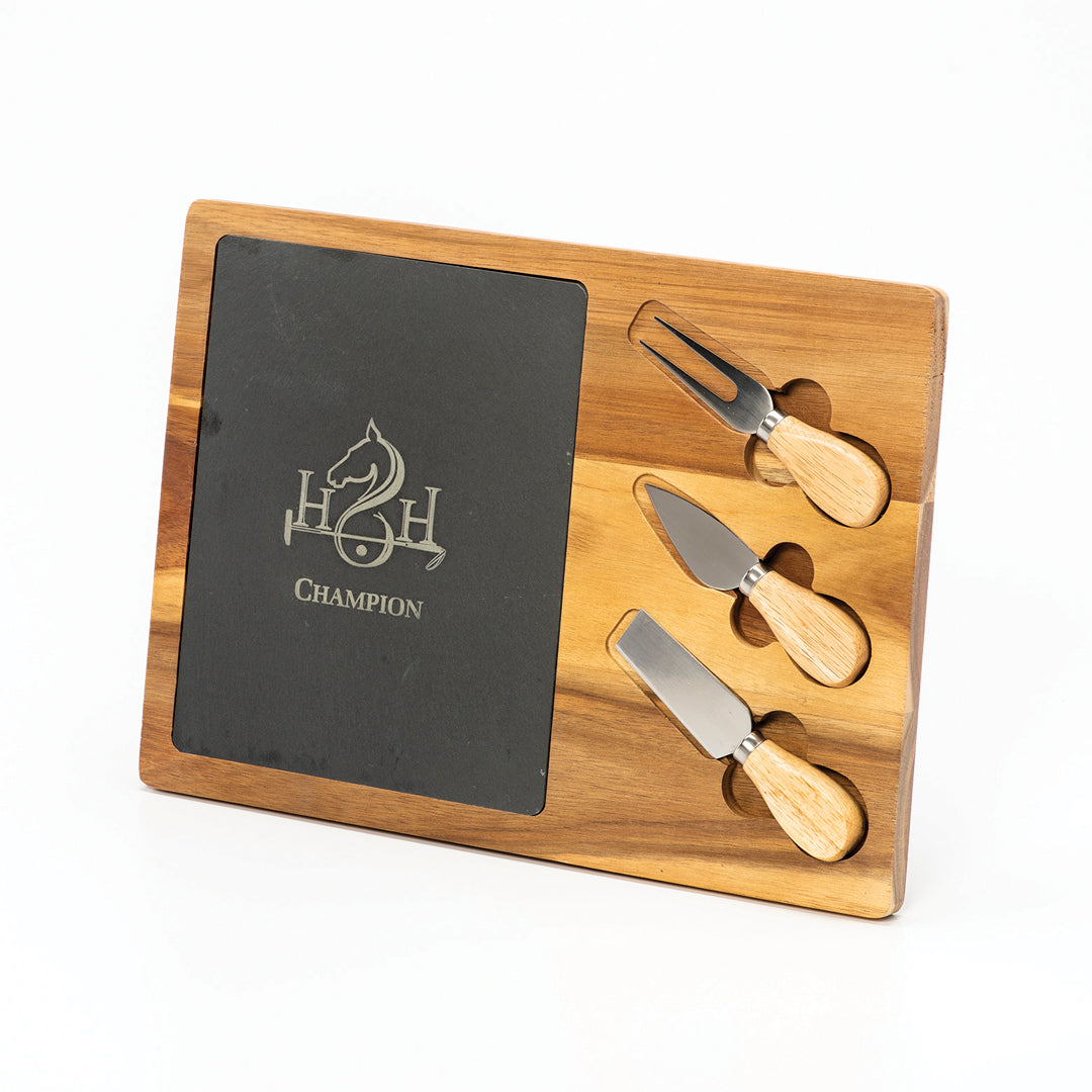 The Prize Possessions Wood/Slate Cheese Set with Tools features a horse logo and “CHAMPION,” plus three wooden-handled cheese knives and a fork that fit into side slots—ideal for serving at gatherings.
